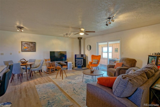 living area featuring a textured ceiling, rail lighting, ceiling fan, wood finished floors, and a wood stove
