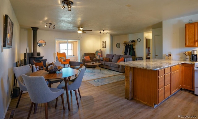 interior space with a peninsula, a ceiling fan, a wood stove, and light wood-type flooring