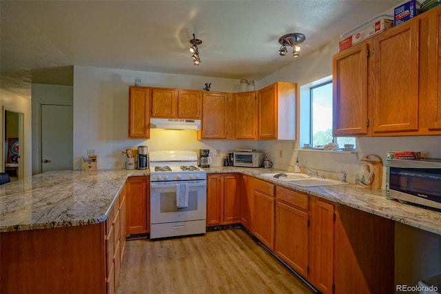 kitchen featuring white gas range oven, a sink, a peninsula, under cabinet range hood, and light wood-style floors