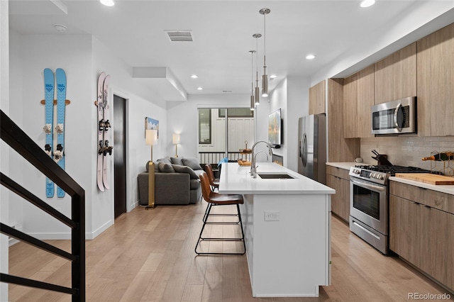 kitchen featuring stainless steel appliances, light countertops, a sink, modern cabinets, and a kitchen bar