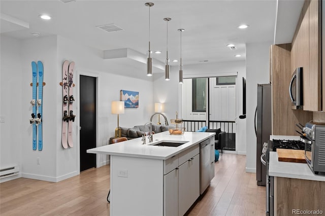 kitchen with a sink, light countertops, appliances with stainless steel finishes, light wood finished floors, and an island with sink