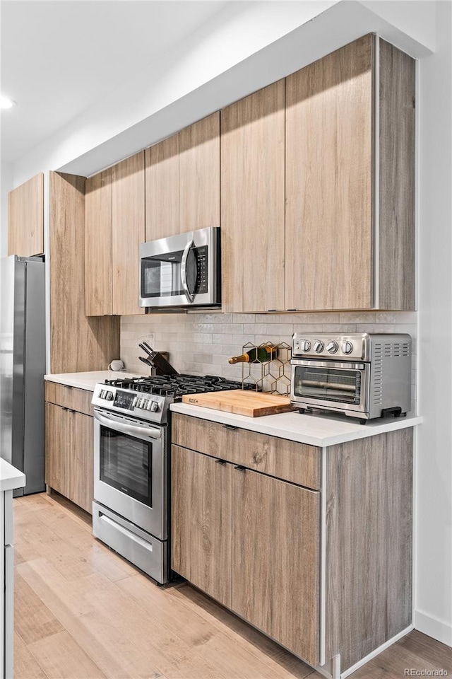 kitchen featuring a toaster, light countertops, appliances with stainless steel finishes, light brown cabinetry, and tasteful backsplash