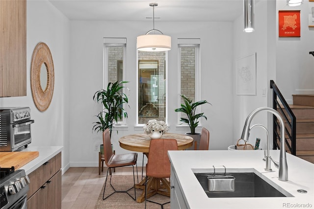 kitchen with decorative light fixtures, a toaster, light countertops, light wood-style flooring, and a sink