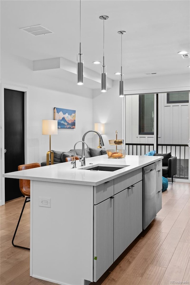 kitchen with a center island with sink, light wood finished floors, stainless steel dishwasher, open floor plan, and a sink