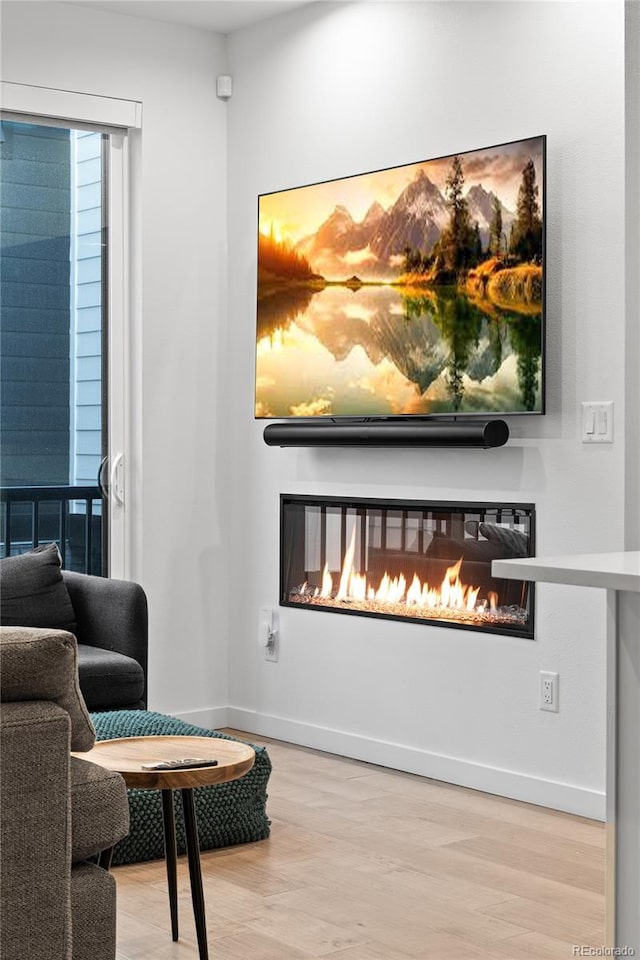 living area featuring a glass covered fireplace, baseboards, and wood finished floors