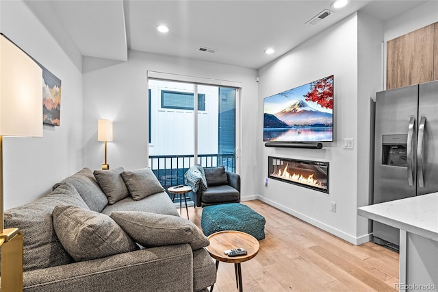 living room featuring light wood finished floors, recessed lighting, visible vents, and a glass covered fireplace