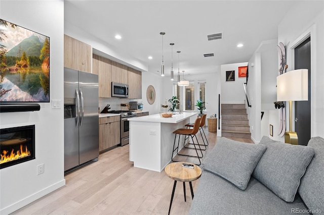 kitchen with a center island, light countertops, visible vents, appliances with stainless steel finishes, and a kitchen breakfast bar