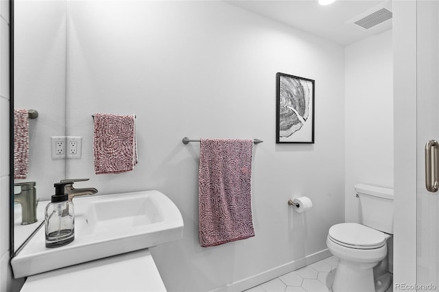 bathroom featuring toilet, a sink, visible vents, baseboards, and tile patterned floors