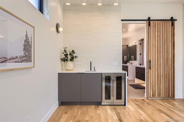 bar with wine cooler, a barn door, baseboards, a sink, and light wood-type flooring