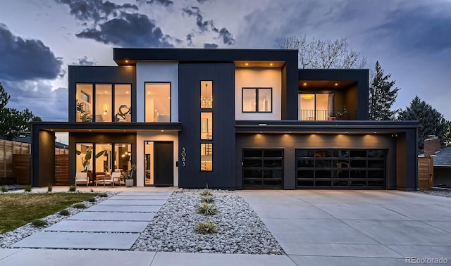 modern home featuring a balcony, driveway, an attached garage, and fence