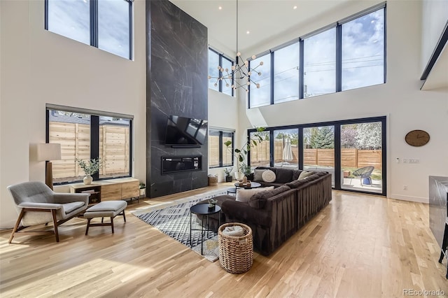 living area featuring a chandelier, a towering ceiling, baseboards, and wood finished floors