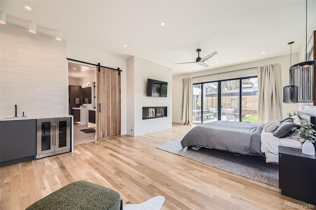 bedroom with a sink, a barn door, access to exterior, recessed lighting, and light wood-style floors