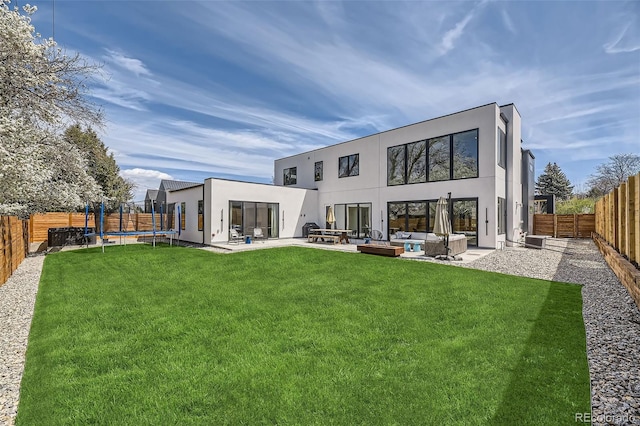 back of property featuring a lawn, a trampoline, a patio area, stucco siding, and a fenced backyard