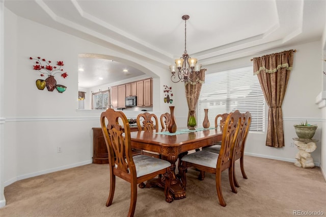 dining space featuring a tray ceiling, light colored carpet, and a notable chandelier