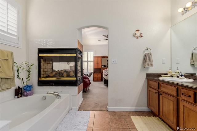 bathroom with ceiling fan, a multi sided fireplace, tile patterned flooring, a bathtub, and vanity