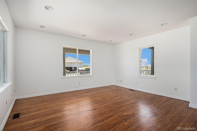 empty room with dark wood-style floors, baseboards, visible vents, and recessed lighting