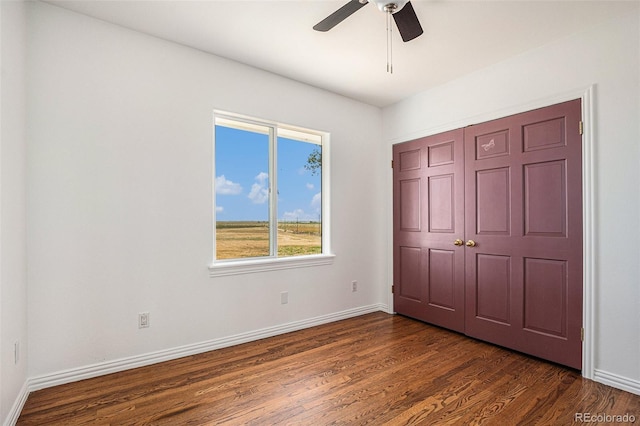 unfurnished bedroom featuring dark wood-style floors, a ceiling fan, baseboards, and a closet