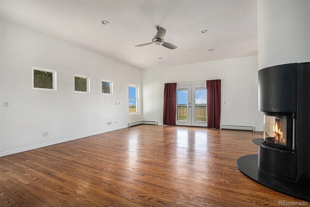 unfurnished living room with dark wood-type flooring, a wood stove, french doors, baseboard heating, and ceiling fan