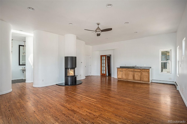 unfurnished living room with dark wood-style floors, a baseboard radiator, a sink, ceiling fan, and baseboards