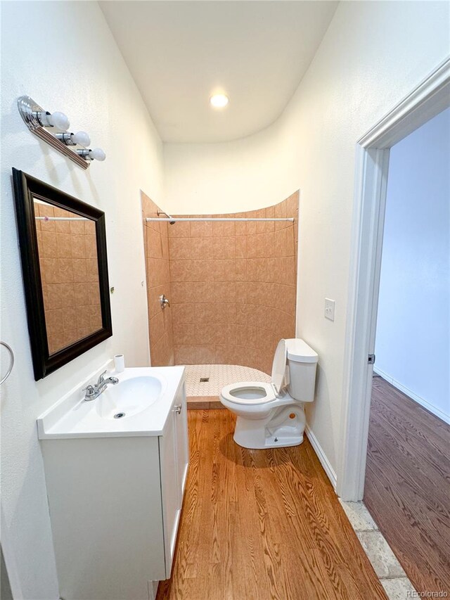 bathroom with hardwood / wood-style floors, toilet, a tile shower, and vanity