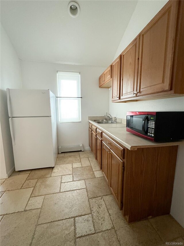 kitchen with sink, a baseboard radiator, light tile patterned floors, vaulted ceiling, and white fridge