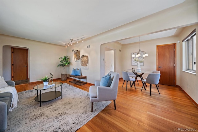 living room with an inviting chandelier, baseboards, light wood-type flooring, rail lighting, and arched walkways