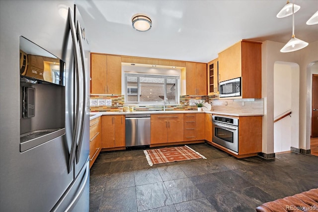kitchen featuring light countertops, arched walkways, a sink, appliances with stainless steel finishes, and backsplash