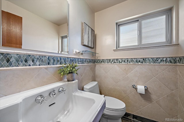 bathroom featuring toilet, tile walls, a sink, and a wainscoted wall