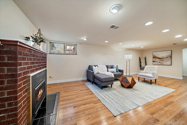 living room featuring a glass covered fireplace, baseboards, light wood finished floors, and visible vents