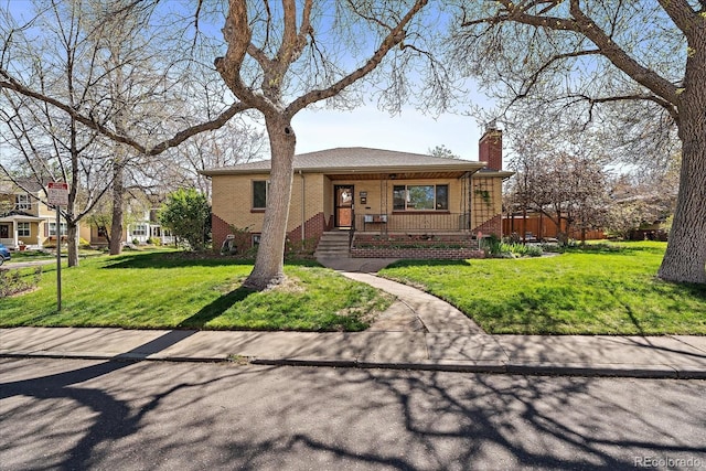 view of front of house featuring a chimney, a porch, a front lawn, and brick siding