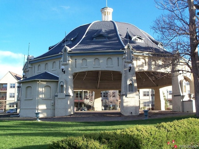 rear view of house with roof with shingles, stucco siding, and a yard