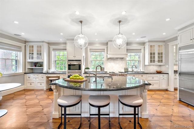 kitchen featuring built in refrigerator, decorative light fixtures, a kitchen island with sink, and sink