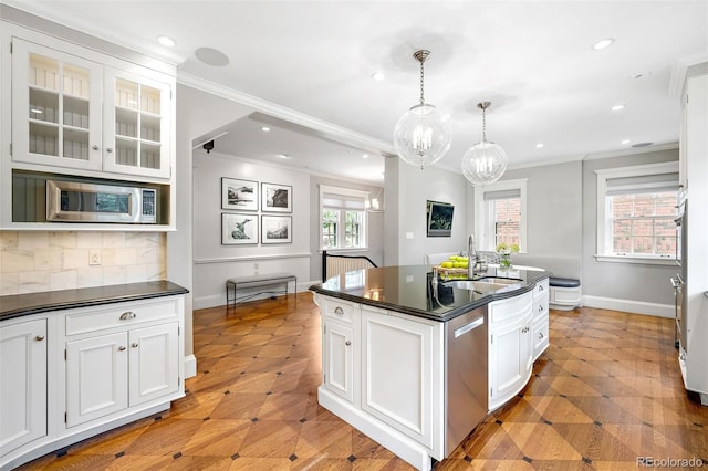 kitchen featuring decorative light fixtures, sink, white cabinets, stainless steel appliances, and a center island with sink