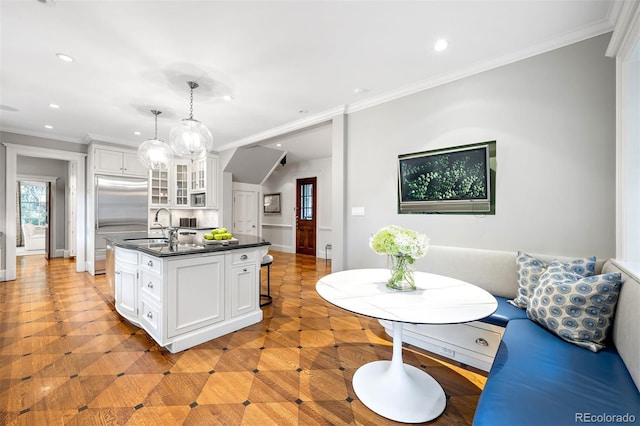 kitchen featuring decorative light fixtures, ornamental molding, breakfast area, a kitchen island with sink, and white cabinets