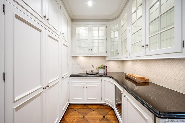 kitchen featuring sink, ornamental molding, white cabinets, decorative backsplash, and dark stone counters