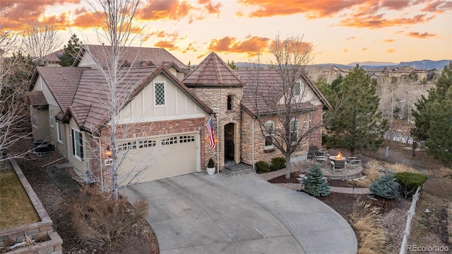 view of front of home with a fire pit, brick siding, concrete driveway, stone siding, and board and batten siding