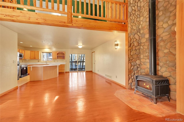 unfurnished living room featuring visible vents, a wood stove, a sink, light wood-type flooring, and baseboards