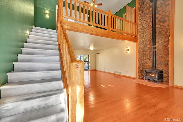 stairway featuring baseboards, visible vents, wood finished floors, a wood stove, and a high ceiling