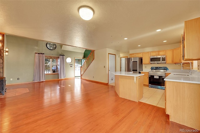 kitchen featuring appliances with stainless steel finishes, open floor plan, a center island, light brown cabinetry, and a sink