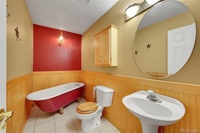 full bath featuring a textured wall, toilet, wainscoting, a sink, and a freestanding tub