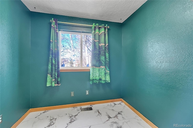 spare room with marble finish floor, visible vents, a textured wall, a textured ceiling, and baseboards