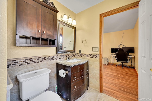 half bathroom featuring wainscoting, toilet, wood finished floors, vanity, and tile walls