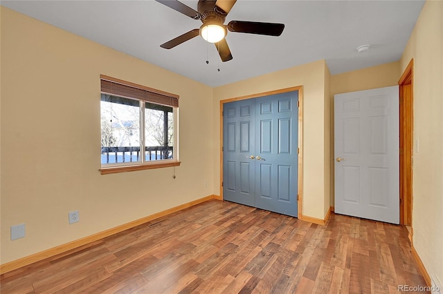 unfurnished bedroom with a closet, visible vents, a ceiling fan, wood finished floors, and baseboards