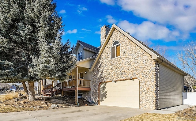 view of side of home with a porch, a garage, driveway, stone siding, and a chimney