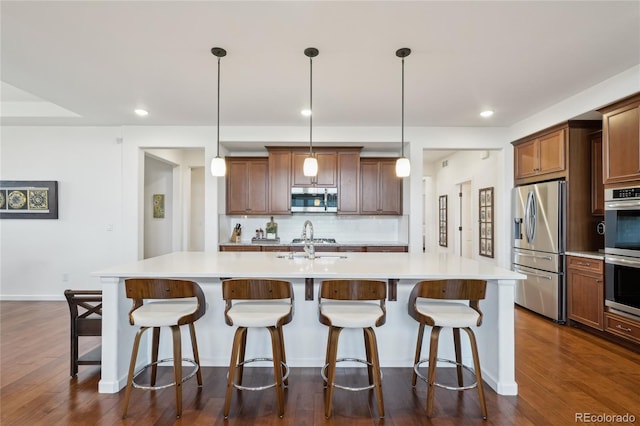 15987 E 115th Pl, Commerce City, CO 80022 - kitchen featuring appliances with stainless steel finishes, backsplash, an island with sink, dark wood-style floors, and recessed lighting