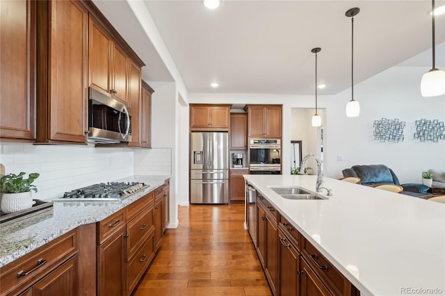 15987 E 115th Pl, Commerce City, CO 80022 - kitchen featuring appliances with stainless steel finishes, a sink, wood finished floors, hanging light fixtures, and decorative backsplash