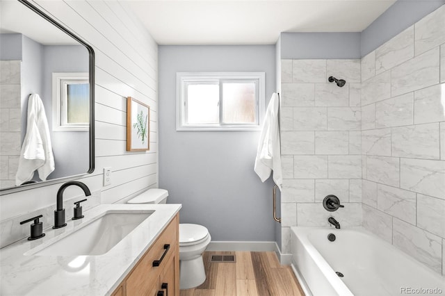 bathroom with toilet, wood finished floors, bathing tub / shower combination, baseboards, and vanity