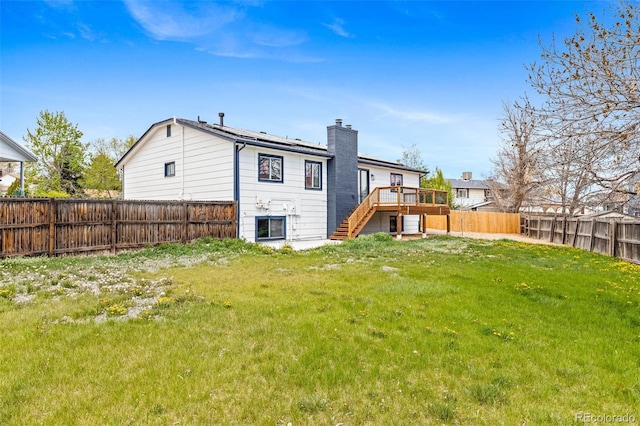 back of house featuring a chimney, a lawn, a deck, stairway, and a fenced backyard