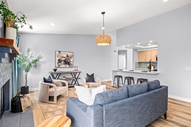 living room with a brick fireplace, baseboards, recessed lighting, and light wood-type flooring