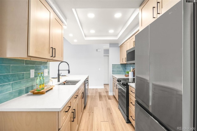 kitchen featuring appliances with stainless steel finishes, a sink, light wood-style floors, a tray ceiling, and backsplash
